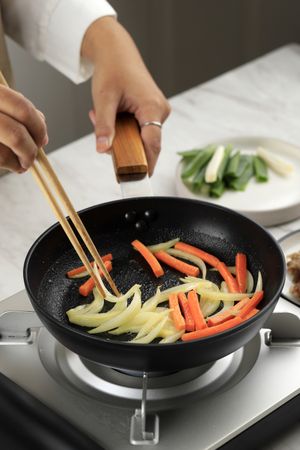 Female Hand Sauteed Onion and Carrot on Black Pan