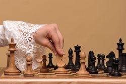 Hand in lace blouse moving chess piece on board.