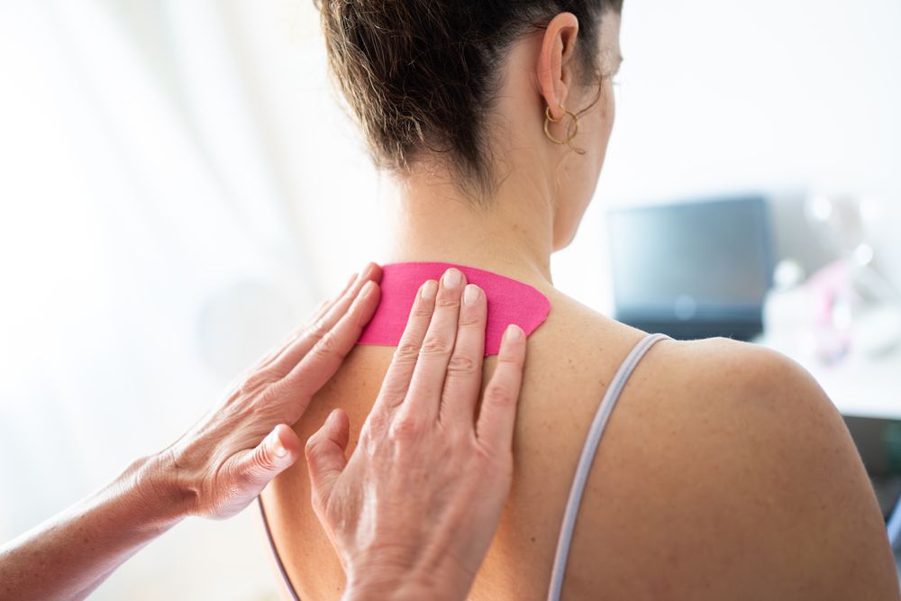 Physical therapist using kinesiology tape on upper back of patient