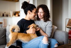 Female couple sitting close by and relaxing at home on sofa with dog