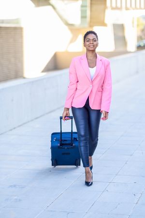 Black woman walking with travel bag wearing pink jacket