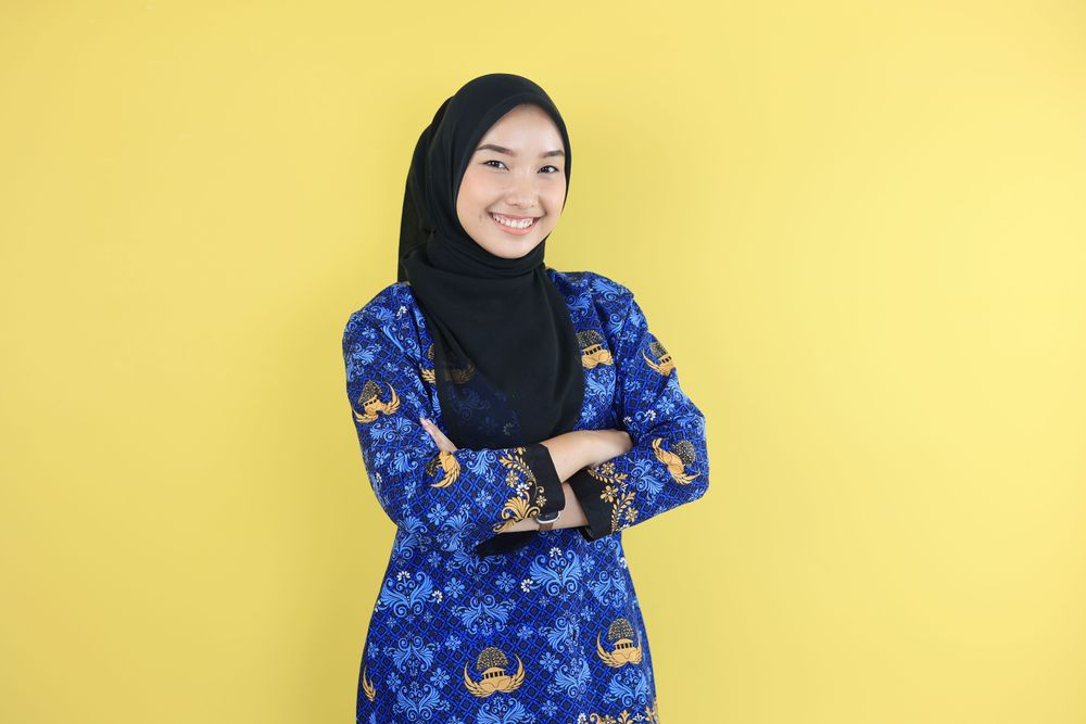 Woman in Hijab and Korpri Batik Blue Uniform Showing Confident Gesture by Folding Her Arms.