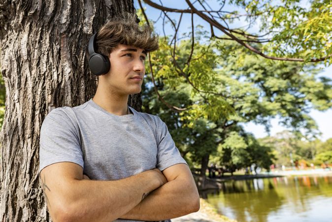 A young man listening to music, leaning on a tree with his arms