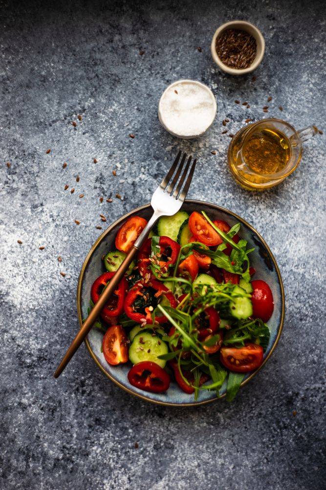 Healthy vegetable salad with organic cucumber, tomatoes, bell pepper, arugula and flax seeds on grey table