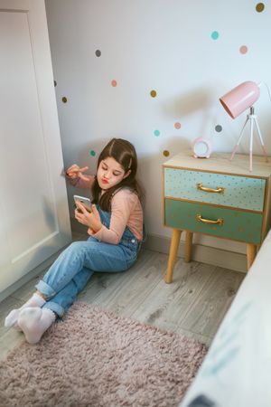 Girl with duck face taking selfie with cell phone for social media sitting on the floor