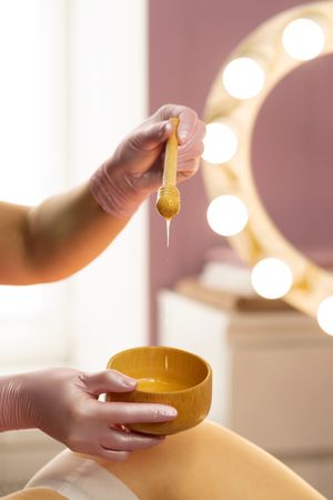 Honey slowly dripping from wooden stick during spa session.