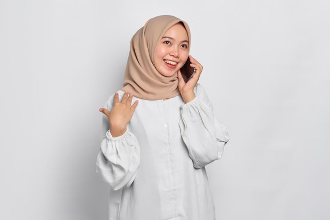Happy Asian Muslim woman talking on cell phone with hand on her shoulder