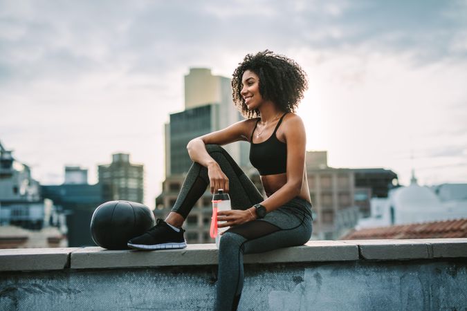 Smiling woman in fitness clothes relaxing after workout sitting on rooftop