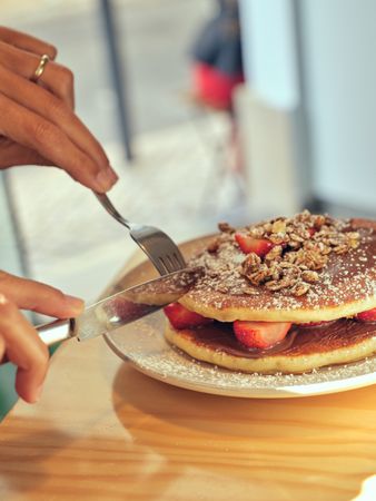Faceless person cutting pancakes with strawberries