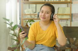 Young woman in the yellow shirt is listening to music  an app on smartphone at home.