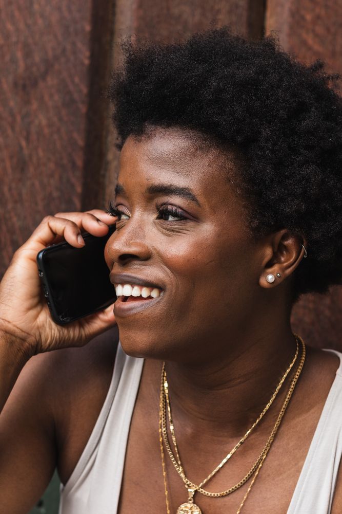 Smiling Black woman talking on smartphone sitting near building