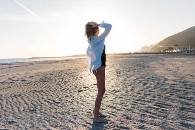 Woman with her arms up on beach in oversized shirt