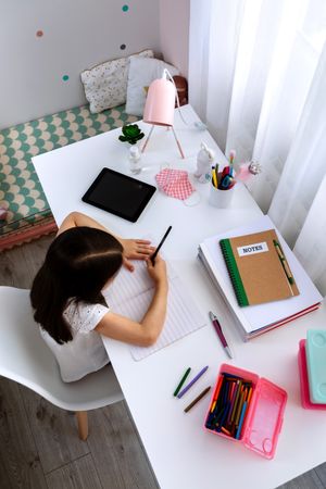 Girl studying at home with tablet and mask on table