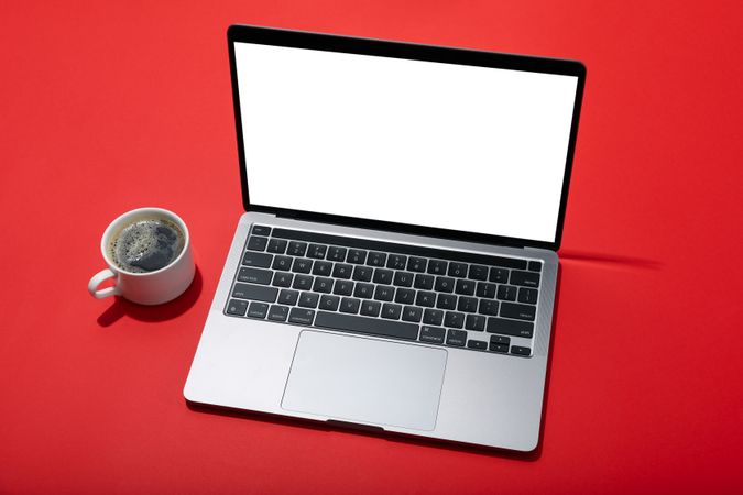 Top view of laptop keyboard with blank screen on red table with coffee