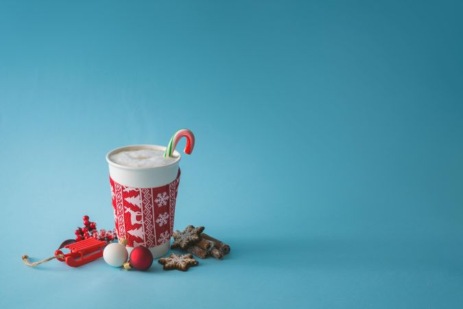 To-go cup of coffee with Christmas sleeve and candy cane, decorations and cookies
