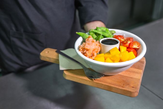 Unrecognizable chef showing freshly prepared colorful poke bowl with salmon on restaurant kitchen
