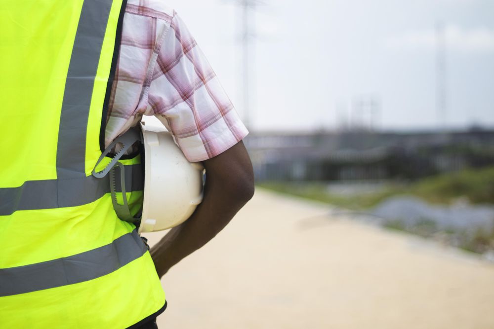 Back view of man in green vest holding a bump cap under his arm
