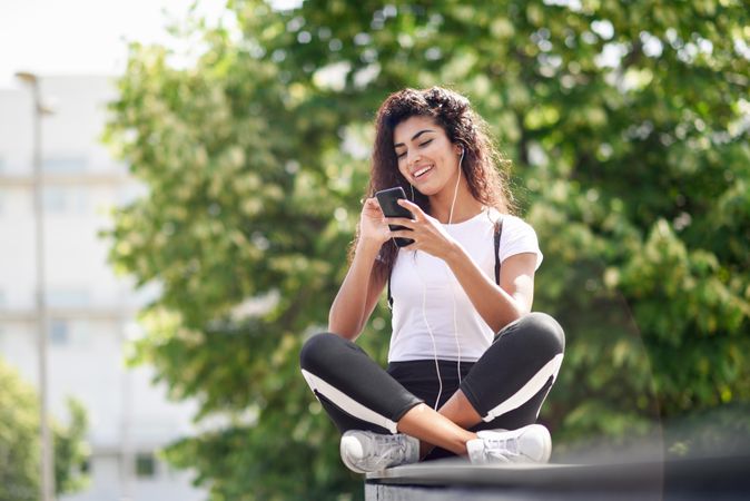 Arab woman smiling while using phone sitting outdoors