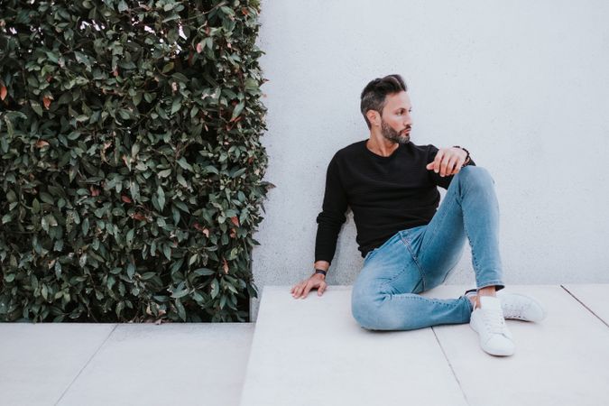 Adult stylish man sitting near grey wall