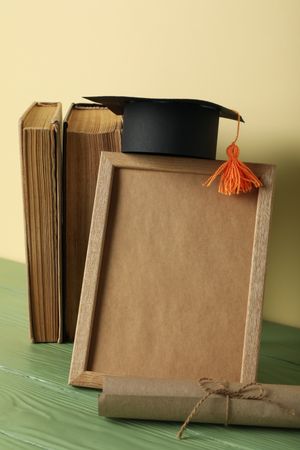 Frame and graduate hat with books on table.