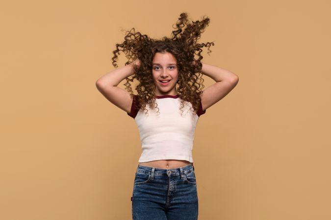 Playful young girl lifting hair with both hands, smiling energetically