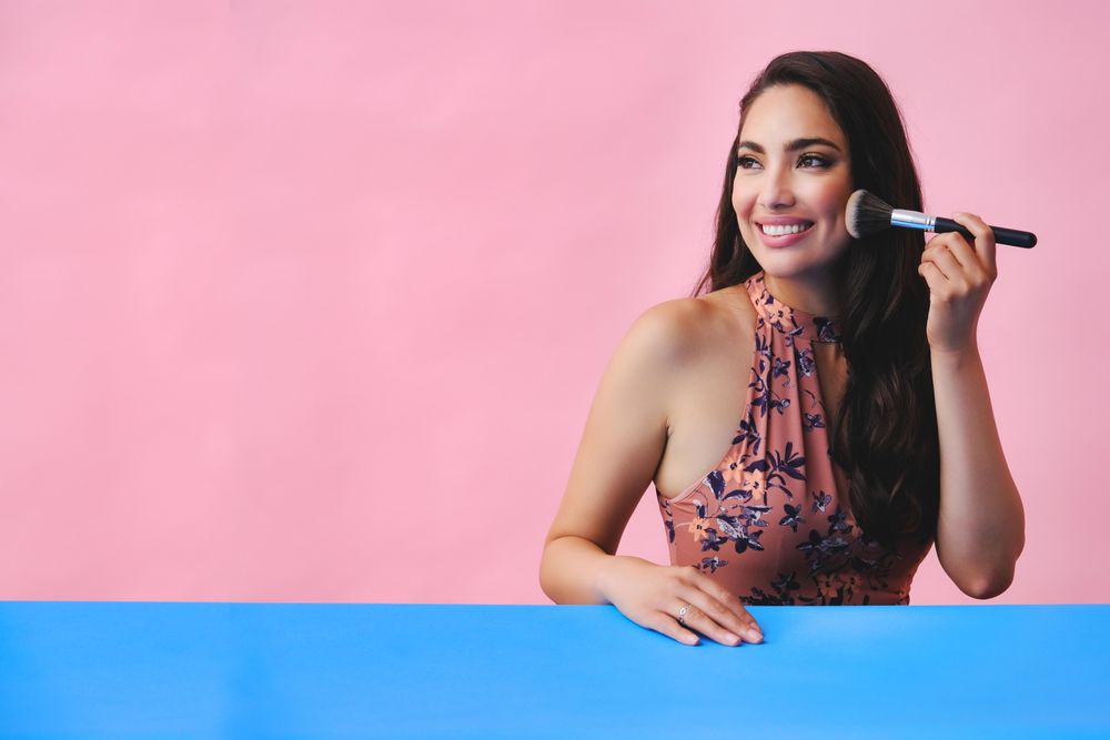 Smiling Hispanic woman with long brown hair holding large make up brush, copy space