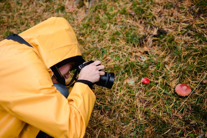 Person in yellow raincoat photographing mushrooms