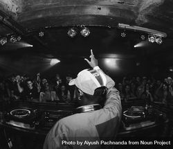 Fisheye shot from behind young DJ on stage holding hand up to audience 4d8nr4