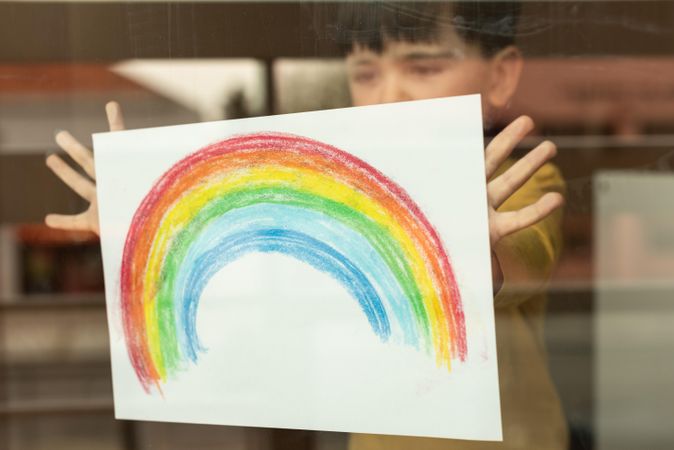 Boy showing rainbow drawing from window glass