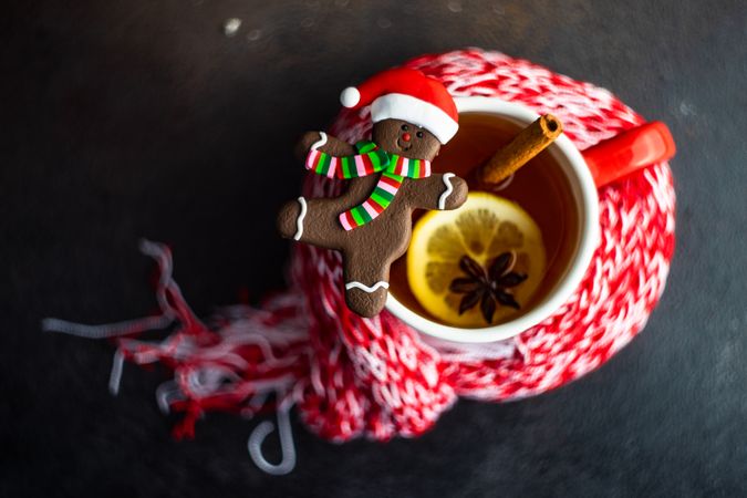 Top view of cup of mulled tea wrapped in red scarf with gingerbread cookie