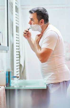 Man shaving beard with razor in bathroom