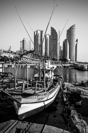 Grayscale photo of boat on water near city buildings in Busan, Busan, South Korea