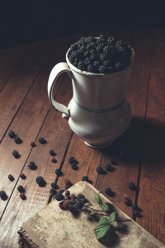 Vintage jag with ripe blackberries on wood and leaves on a old book