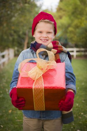 Young Boy Wearing Holiday Clothing Holding Christmas Gift Outside