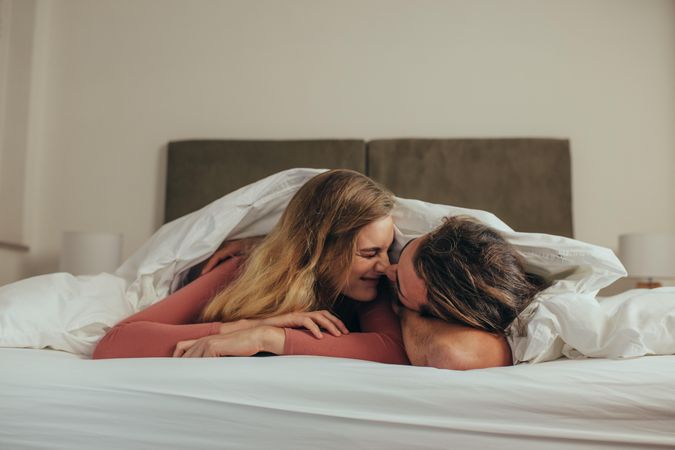 Couple lying on bed at home romancing by touching their noses