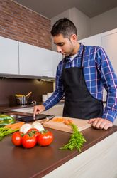 Man checking digital tablet for recipe as he prepares dinner