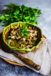 Georgian chakapuli stew on counter served with fresh herbs and spoon