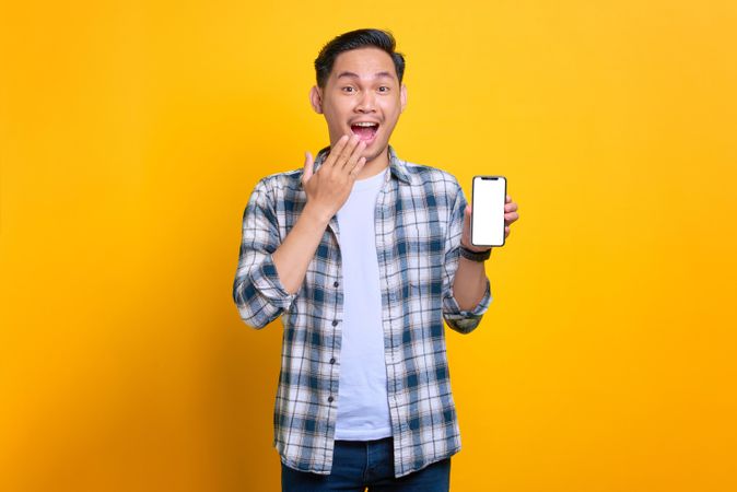 Asian male with hand over mouth and showing blank screen of smart phone
