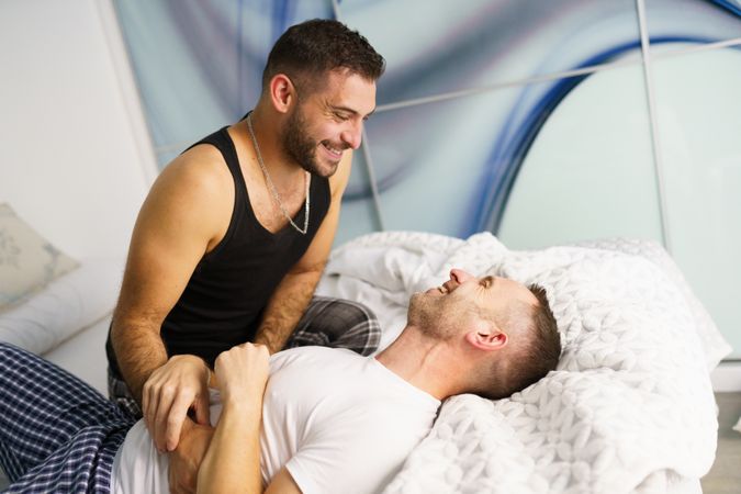 Male couple tickling each other playfully in bed together