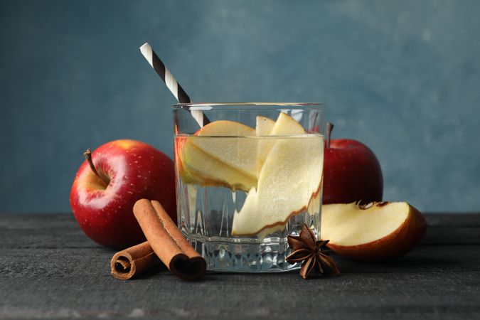 Sideview of glass of water with straw, apple slices and cinnamon slices