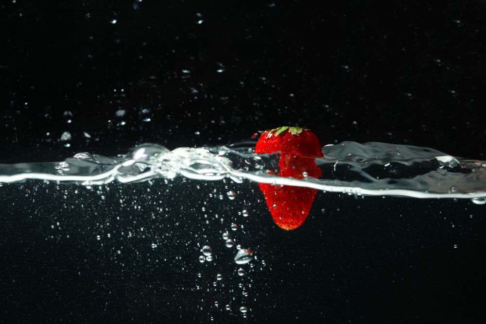 Side view of water on dark background with a suspended strawberry