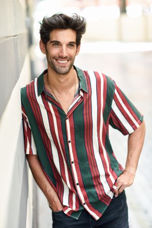 Portrait of man with dark hair smiling outside leaning on wall