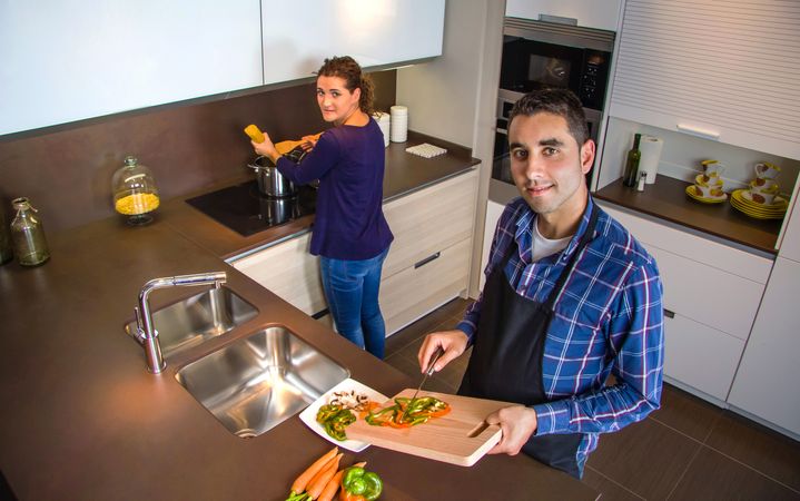 Couple looking up at camera while cutting vegetables in the kitchen preparing food