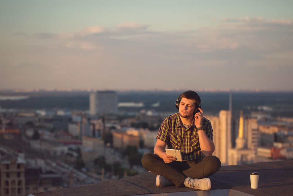 Male using digital tablet with headphones with takeaway coffee cup on roof over city