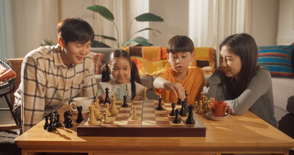 Happy Korean Family Spending a Weekend Evening at Home Together: Father and Son Playing a Game of Chess While Mother and Daughter are Watching.