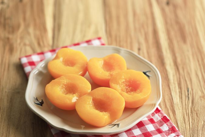 Plate of tinned peaches on wooden table with checkered napkin