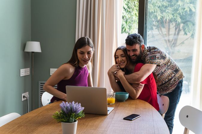 Happy friends hugging and using laptop at dining table