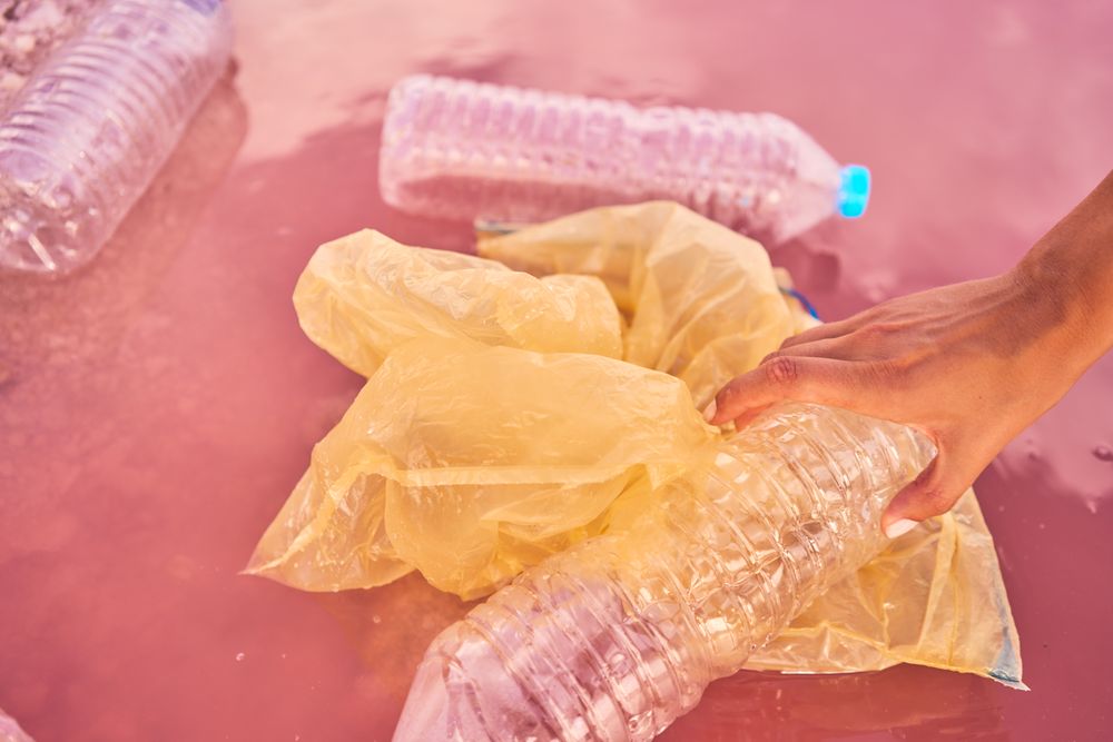 Crop hand touching plastic rubbish in polluted sea water