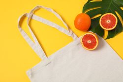 Eco bag, palm leaf and orange on color background, copy space