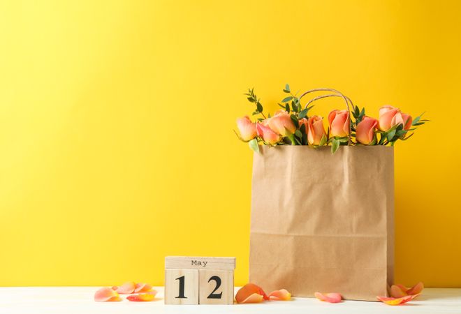 Paper bag with bouquet of orange roses and calendar on table against color background, space for text